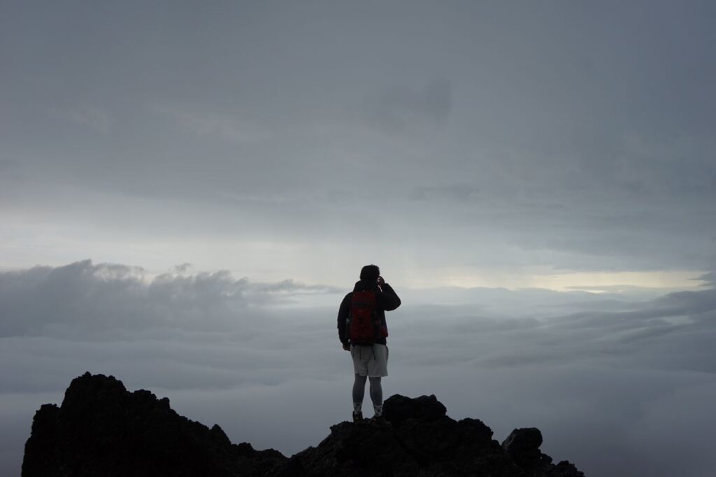 A lone climber stands on a mountain peak above the clouds, embracing adventure and solitude.
