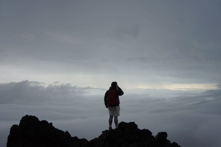 A lone climber stands on a mountain peak above the clouds, embracing adventure and solitude.