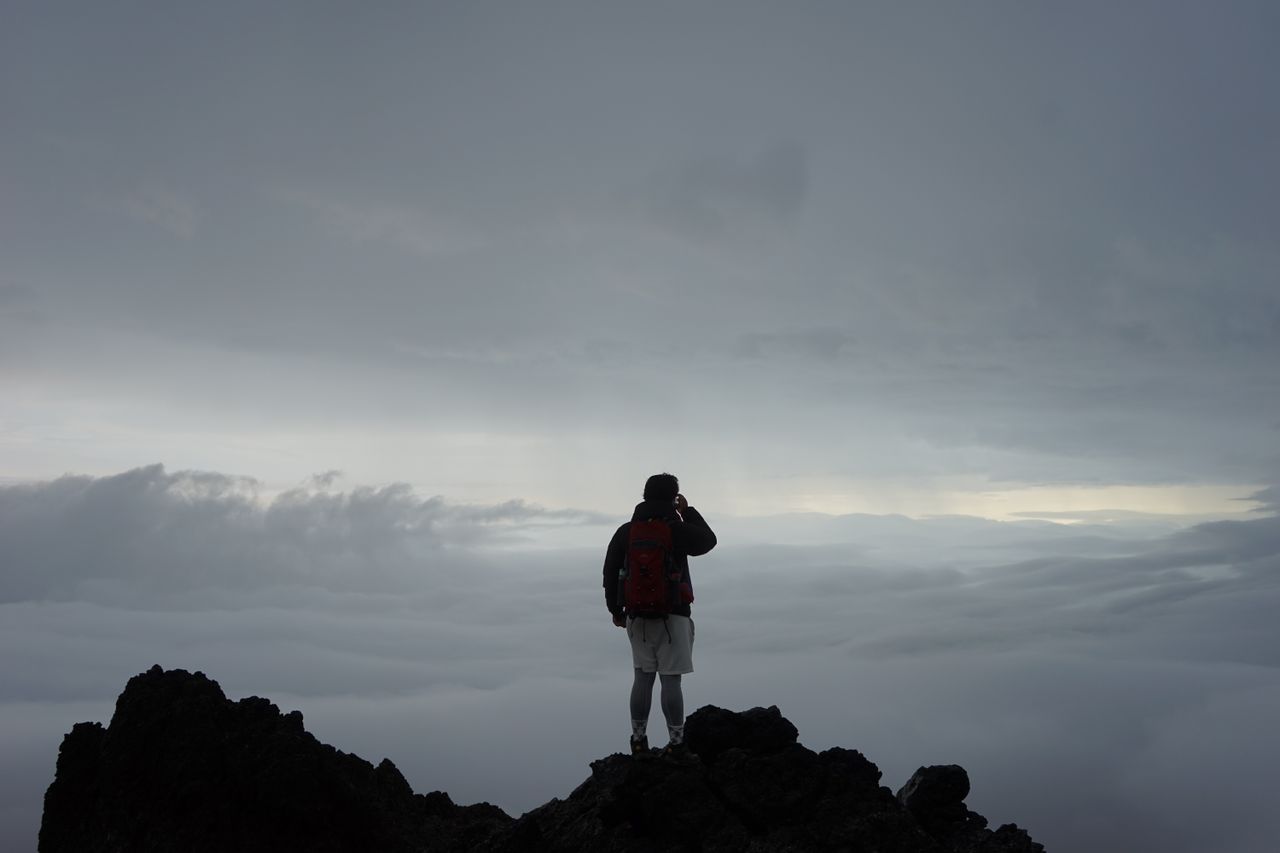 A lone climber stands on a mountain peak above the clouds, embracing adventure and solitude.
