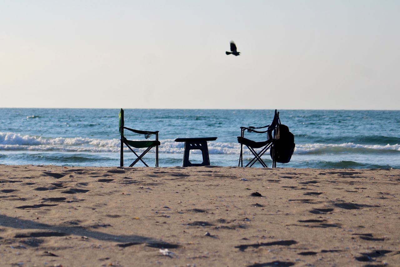 Empty beach chairs facing the serene ocean with waves breaking gently on a sunny day.