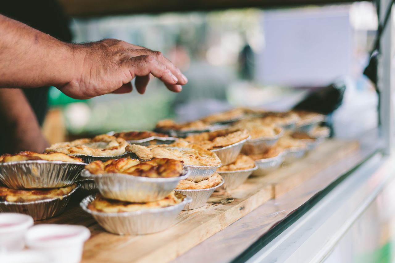 Hand reaching for delicious freshly baked pies at an outdoor market in Rotorua.