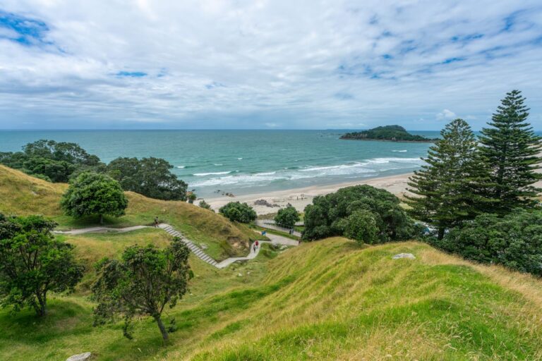Breathtaking coastal landscape of Mount Maunganui, showcasing lush green hills, sandy shores, and vibrant blue sea.