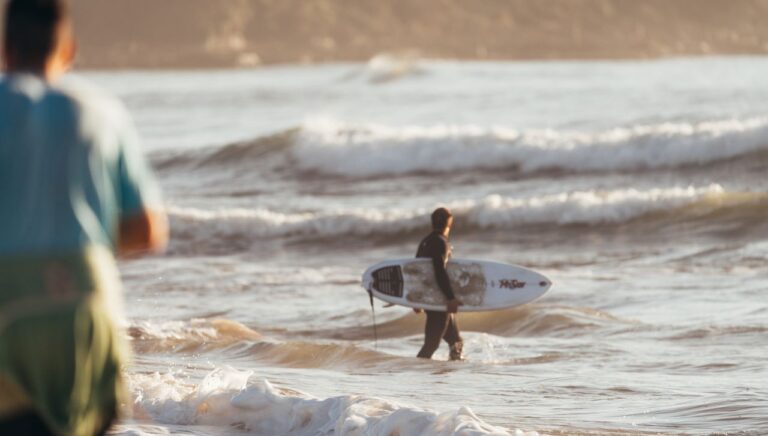 Side view of anonymous man with surfboard watching waves and preparing for practising surfing